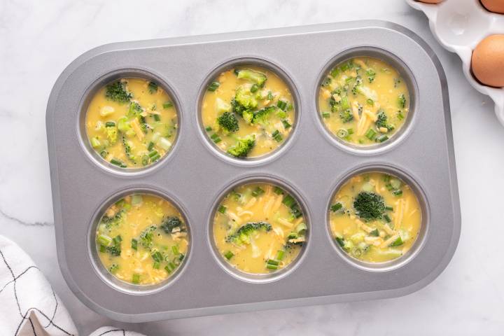 Egg muffins with broccoli and cheese in a muffin tin before baking