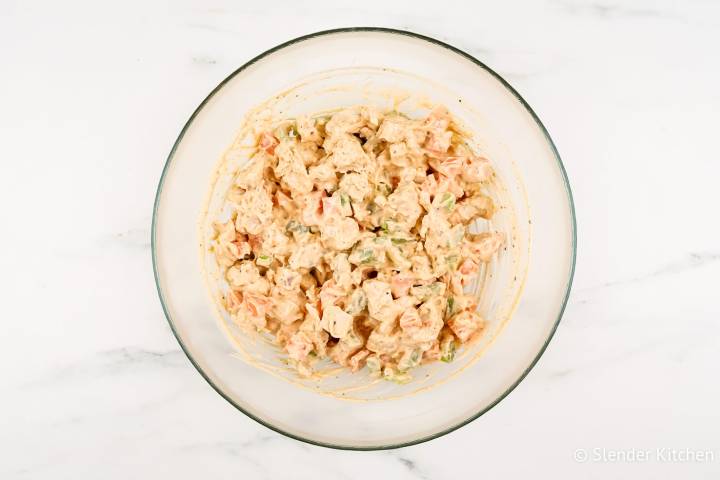 Buffalo chicken salad mixed together in a glass bowl with carrots and celery.