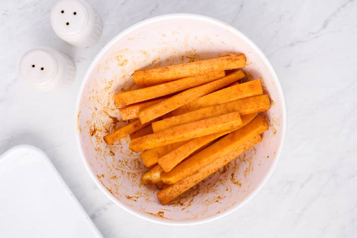 Butternut squash sticks tossed with olive oil and spices in a bowl.