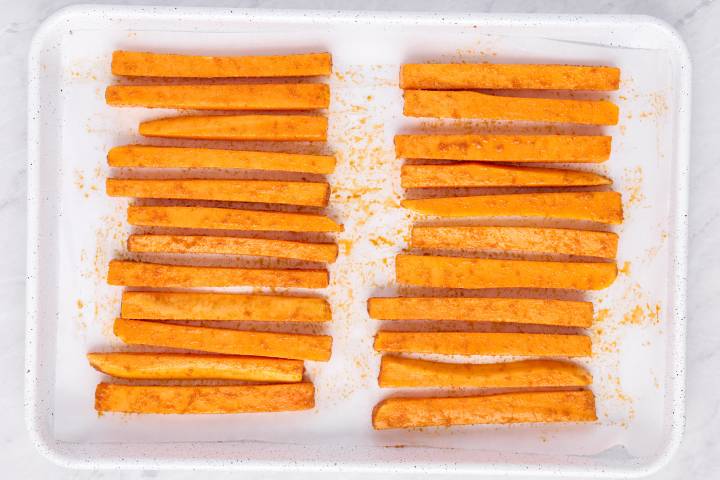 Raw butternut squash fries tossed with spices on a baking sheet.