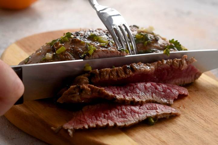Grilled carne asada being sliced with a knife into thin slices/