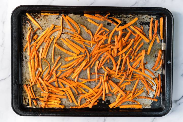 Baked carrot fries with crispy edges on a baking sheet.