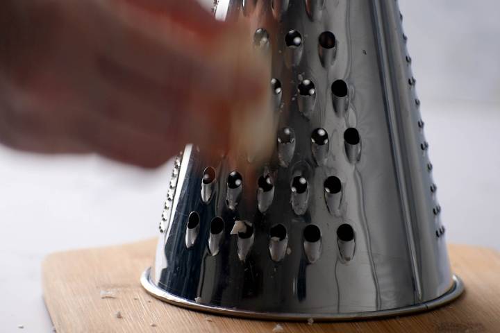 Cauliflower being grated into rice on a box grater.