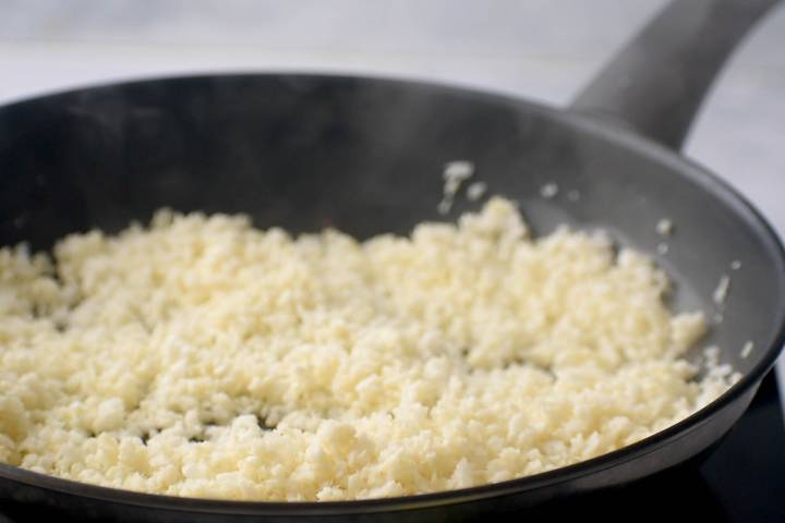 Cauliflower rice being sauteed in a pan with olive oil.