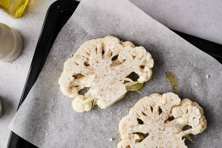 Raw cauliflower steaks seasoned with salt, pepper, and olive oil on a parchment-lined baking sheet.