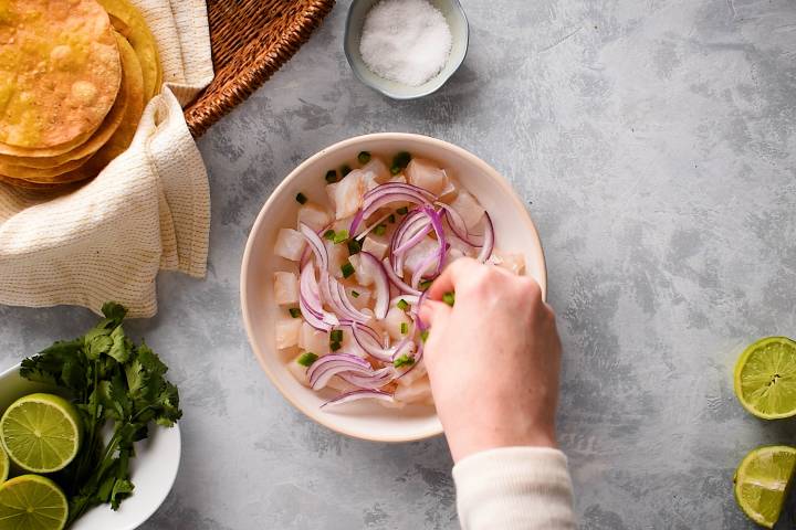 Raw fish in a white bowl with red onions and jalapenos.