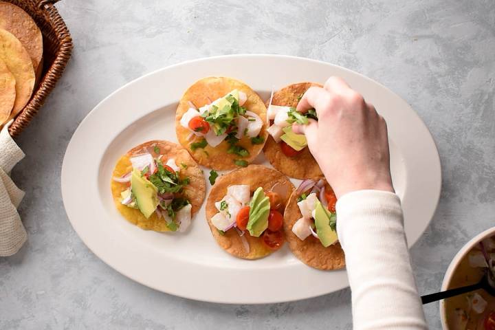 Ceviche tostadas on a plate with cilantro being sprinkled on top.