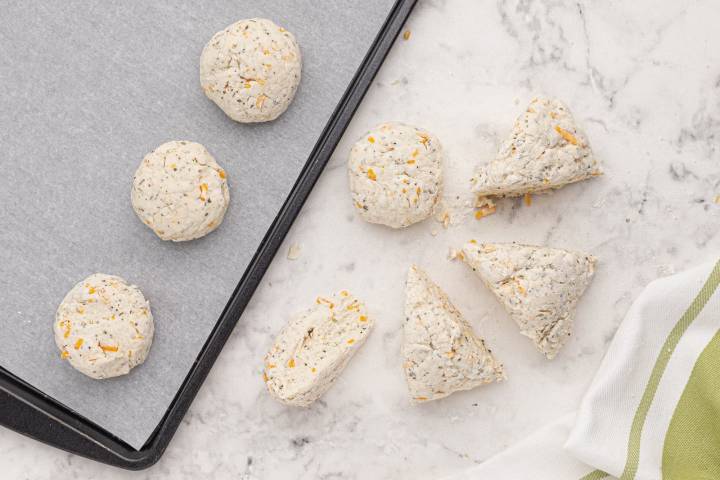 Biscuit dough being formed into round biscuits on a baking sheet.