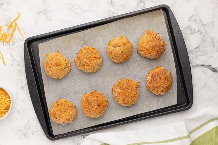 Golden brown cheddar biscuits on a baking sheet.