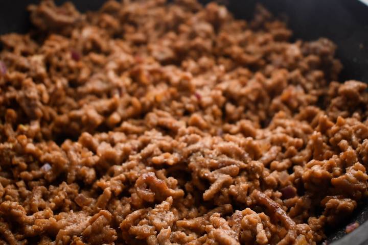Ground beef cooking in a skillet with red onions.