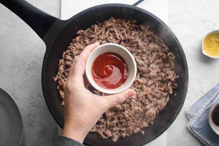 Ketchup being adding to a skillet of ground beef.