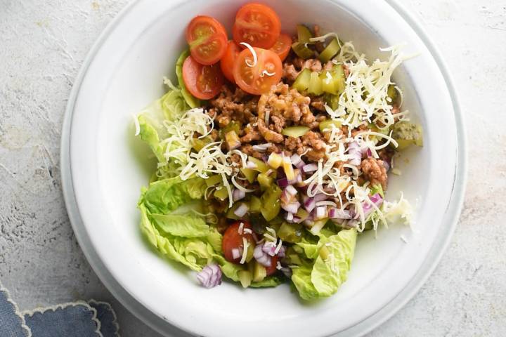 Cheeseburger salad being assembled with tomatoes, meat, and lettuce.