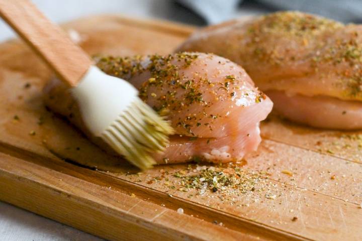Chicken breasts being brushed with olive oil and seasoning.