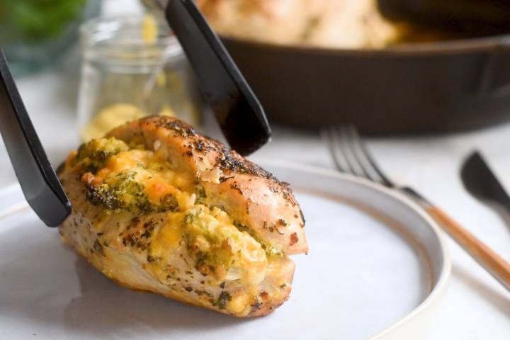 Stuffed broccoli cheddar chicken breasts being putting on a plate with tongs.
