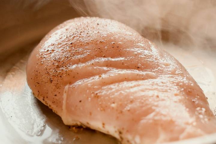 Chicken breast searing in a pan with salt and pepper.