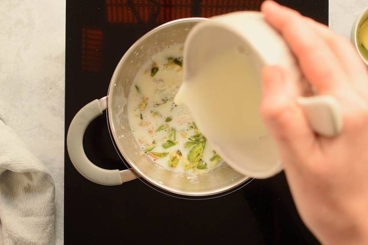 Evaporated milk being added to jalapenos in a pot to make cream sauce.