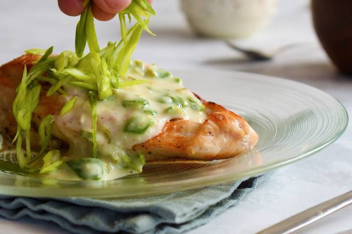 Chicken with jalapeno cream sauce on a plate with green onions and lemon on top.