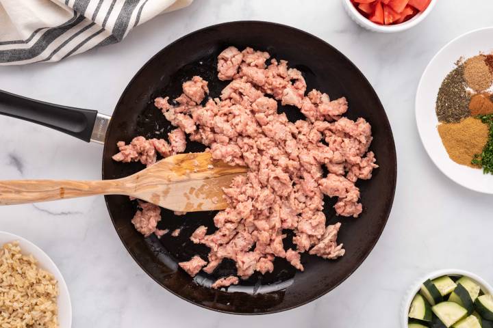 Ground chicken cooking in a skillet with a wooden spoon.