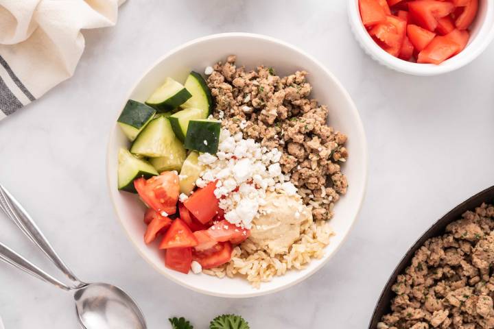Chicken kofta bowls with brown rice, hummus, tomatoes, cucumbers, and feta cheese. 
