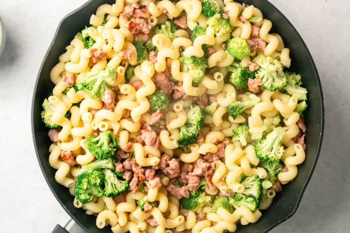 A skillet filled with corkscrew pasta mixed with crispy broccoli and savory sausage pieces, creating a colorful and hearty dish.