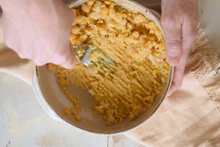 Chickpeas being mashed in a bowl with a fork.