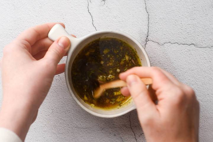 Greek vinaigrette with olive oil, red wine vinegar, lemon juice, garlic, and oregano being stirred together.