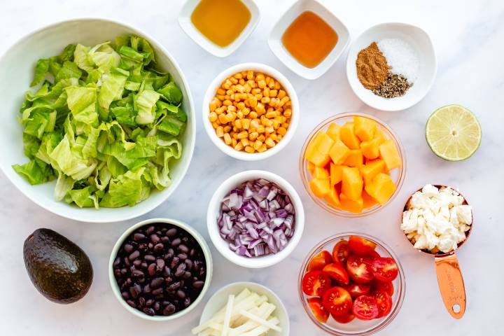 Ingredients for Mexican chopped salad including lettuce, mango, black beans, tomatoes, corn, and more.