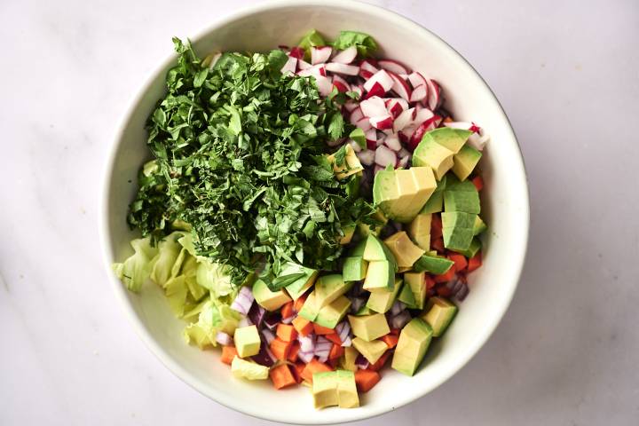 A top-down shot of a bowl with chopped shrimp, bell peppers, avocado, corn, and cilantro.