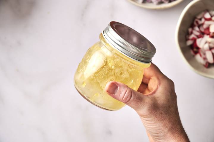 A top-down shot of a person mixing a bowl of chopped shrimp salad with a spoon.