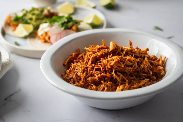 Cochinita pibil in a bowl with tacos on the side.