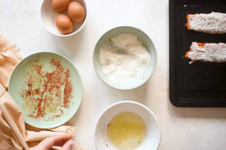 Salmon being coated with spices, eggs, and shredded coconut.