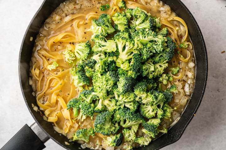 A black skillet holds fettuccine pasta and vibrant broccoli florets in a creamy sauce, creating a warm, appetizing, and comforting dish.