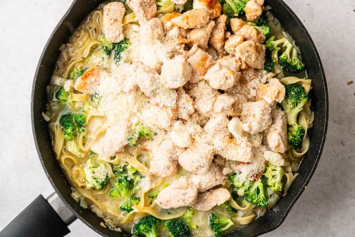 A skillet filled with creamy pasta, vibrant broccoli, and chunks of golden-brown chicken, sprinkled with grated cheese for a hearty, comforting meal.