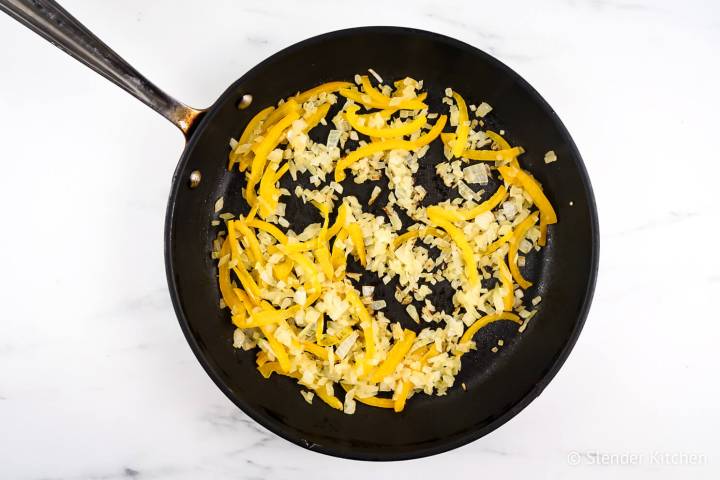 Bell peppers and onions being cooked in a pan.