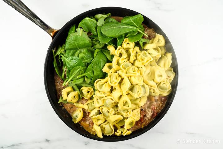 Chicken tortellini with fresh spinach in a pan with tomato sauce.