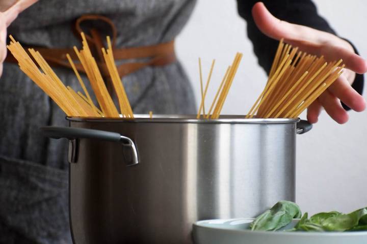 Pasta cooking in a large pot with hands on the side.