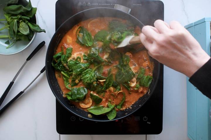 Spinach being stirred into a creamy tomato sauce in a pan.