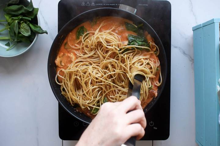 Creamty tomato pasta with spinach and mushrooms being stirred in a pan.