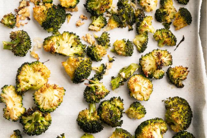 Roasted broccoli florets on a parchment-lined baking sheet, golden and crispy. The image conveys a sense of warmth and appetizing aroma.