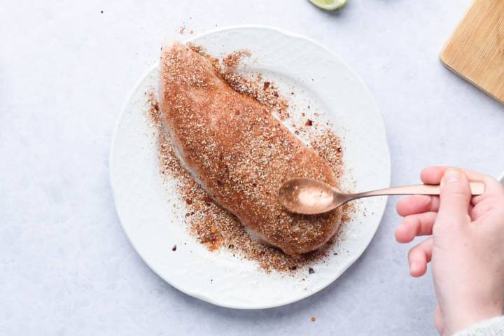Chicken breast being coated with a cumin seasoning rub.