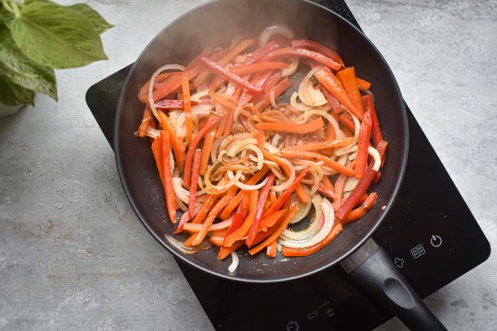 Peppers and onions cooking in a pan.