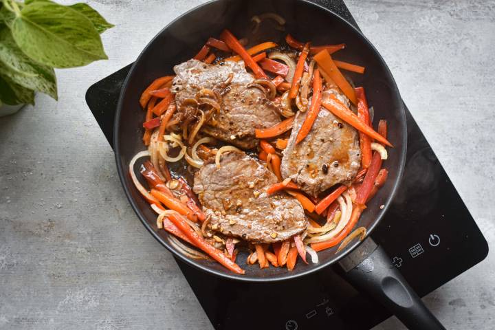 Pepper steak cooking in a pan with peppers and onions. 