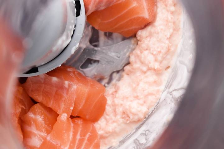 Fresh salmon chunks being added to a food processor.
