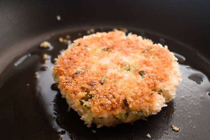 Salmon burgers cooking in a hot skillet with oil