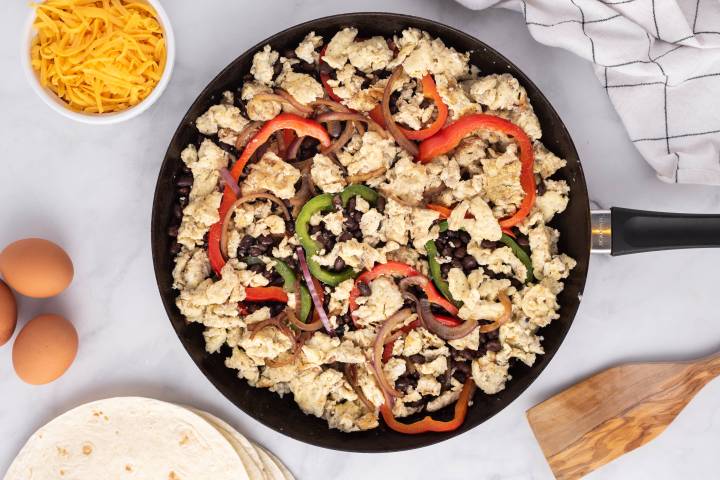 Eggs, beans, peppers, and onions cooking in a skillet for burritos.