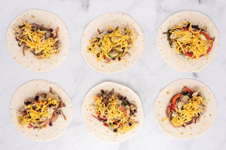 Breakfast burritos being assembled with eggs, cheese, and salsa.