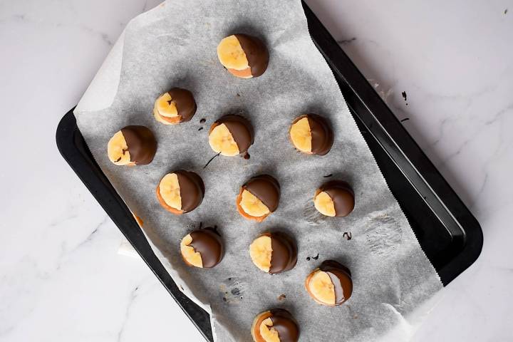 Frozen banana bites dipped in chocolate on a baking sheet.