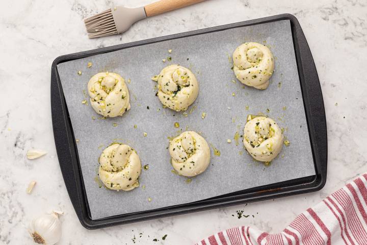 Baking sheet with six garlic knots before being baked.
