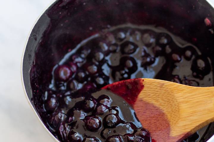 Berry sauce in a small saucepan with wooden spoon.