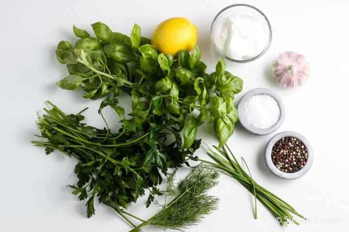 Fresh herbs, lemon, and garlic on a marble board with yogurt.
